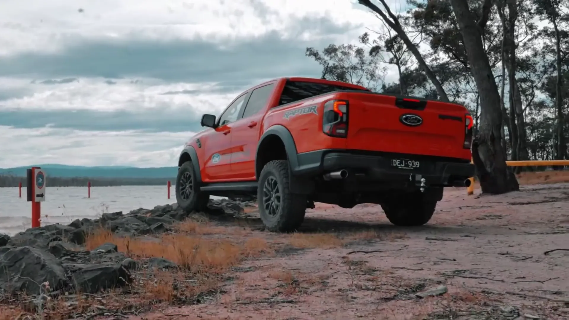An orange Ford Ranger Raptor parked on a lakeside track